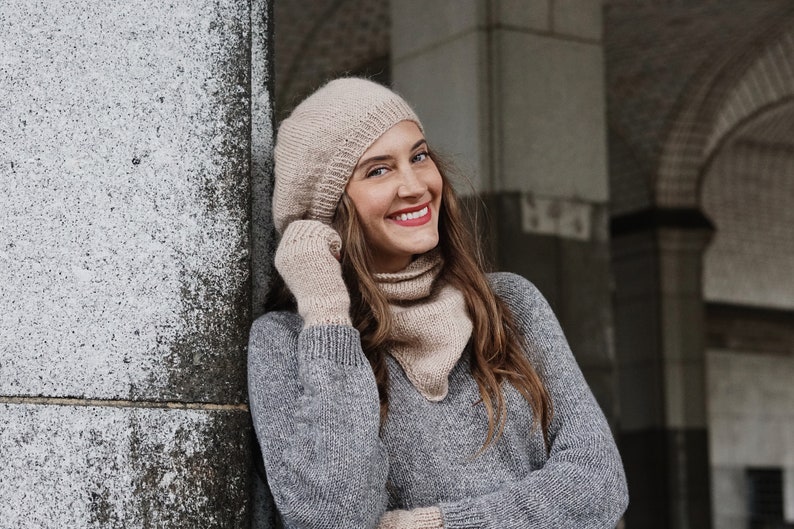 Puede incluir: Una mujer con un su&eacute;ter de punto gris, un gorro de punto beige y una bufanda de punto beige. Est&aacute; sonriendo y mirando hacia la derecha.
