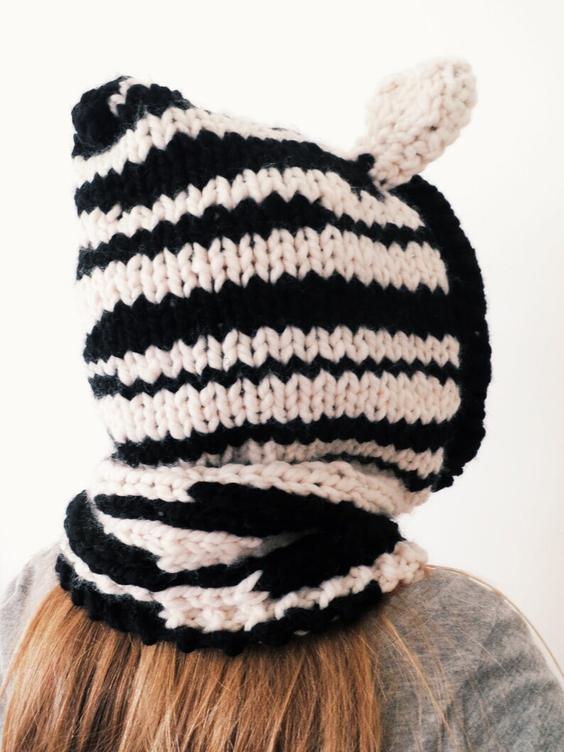 Puede incluir: Un gorro de punto de rayas blancas y negras con orejeras. El gorro est&aacute; hecho de un hilo suave y grueso y tiene una sensaci&oacute;n acogedora y c&aacute;lida.