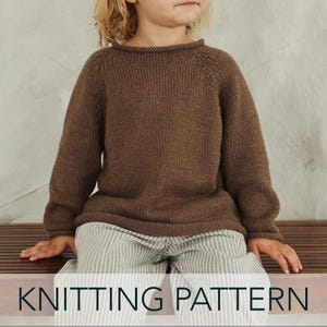May include: A long-sleeved brown knitted sweater with a round neckline and raglan sleeves, paired with light-colored trousers featuring thin vertical stripes. The image includes the text KNITTING PATTERN at the bottom of the frame.