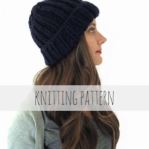 May include: A navy blue knitted beanie hat with a ribbed texture. The hat is worn by a person with long brown hair. The text "KNITTING PATTERN" is displayed below the hat.