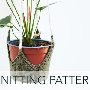 Può includere: Un portavasi in maglia verde con un vaso marrone e una pianta verde con fiori rosa che pendono da esso. Il testo "KNITTING PATTERN" è nella parte inferiore dell'immagine.