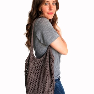May include: A woman wearing a gray t-shirt and blue jeans is carrying a brown knitted mesh tote bag over her shoulder.