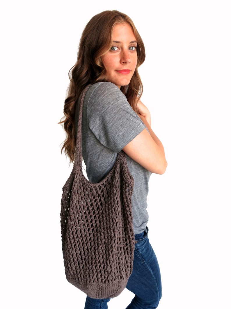 May include: A woman wearing a gray t-shirt and blue jeans is carrying a brown knitted mesh tote bag over her shoulder.
