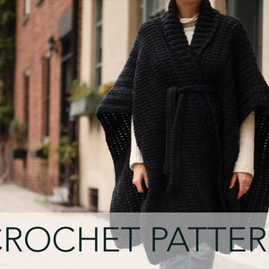 May include: A black crochet poncho with a tie belt. The poncho is worn by a person standing in a city alleyway. CROCHET PATTERN is written in the bottom of the image.