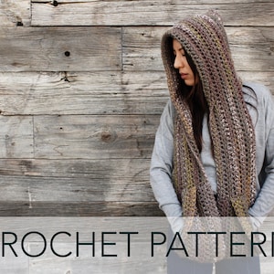 May include: A crochet hooded scarf in brown, beige, and white with a textured pattern. The scarf is worn by a person standing in front of a wooden wall. The text "CROCHET PATTERN" is at the bottom of the image.