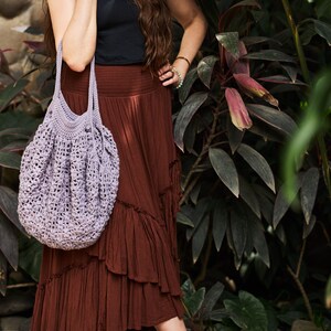 May include: A woman wearing a brown skirt and a black tank top carries a light purple crocheted tote bag.