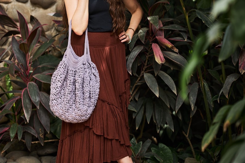 May include: A woman wearing a brown skirt and a black tank top carries a light purple crocheted tote bag.