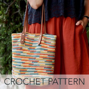 Puede incluir: Un bolso tote de ganchillo multicolor con asas de cuero marrón. El bolso presenta rayas horizontales en tonos azules, amarillos, naranjas y crema. El texto "CROCHET PATTERN" se muestra en la parte inferior de la imagen.