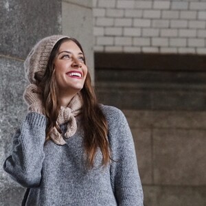 Puede incluir: Una mujer con un su&eacute;ter de punto gris, un gorro de punto beige y una bufanda de punto beige. Est&aacute; sonriendo y mirando hacia arriba.