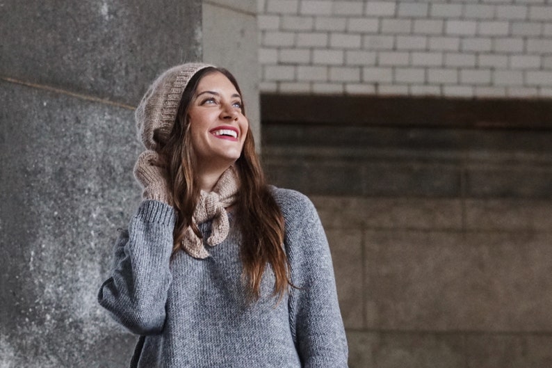 Puede incluir: Una mujer con un su&eacute;ter de punto gris, un gorro de punto beige y una bufanda de punto beige. Est&aacute; sonriendo y mirando hacia arriba.
