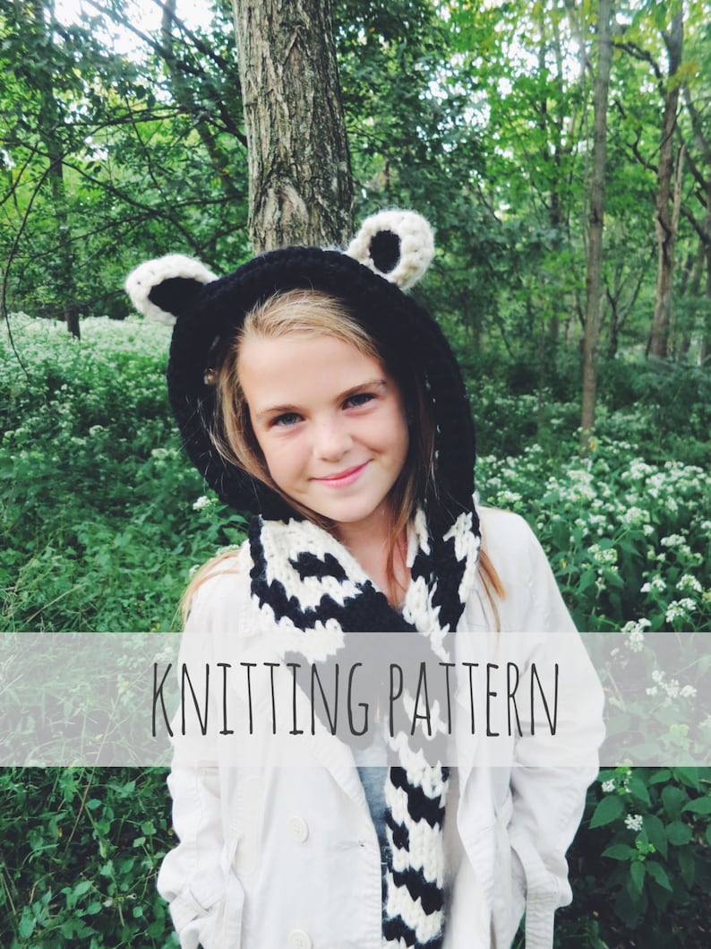 Puede incluir: Una bufanda de punto con capucha a rayas blancas y negras con orejas de oso. La bufanda la lleva puesta un ni&ntilde;o con una chaqueta blanca, de pie en un entorno de bosque. El texto "Knitting Pattern" se muestra en una pancarta blanca.