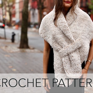 May include: A white crocheted scarf with a fluffy texture, worn around the neck of a person standing on a city street. The text "CROCHET PATTERN" is displayed at the bottom of the image.