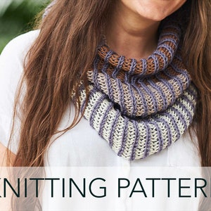 May include: A knitted cowl in shades of cream, lavender, and brown. The cowl is ribbed and has a textured appearance. The text "KNITTING PATTERN" is displayed at the bottom of the image. The cowl is worn around the neck.