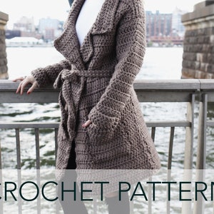 May include: A brown crocheted cardigan with a shawl collar and a tie belt. The cardigan is worn by a person standing on a bridge. The text "CROCHET PATTERN" is at the bottom of the image.