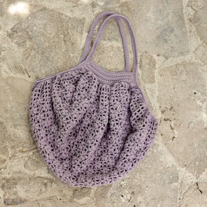 May include: A light purple crocheted tote bag with two handles. The bag is made of a delicate, open-weave pattern.