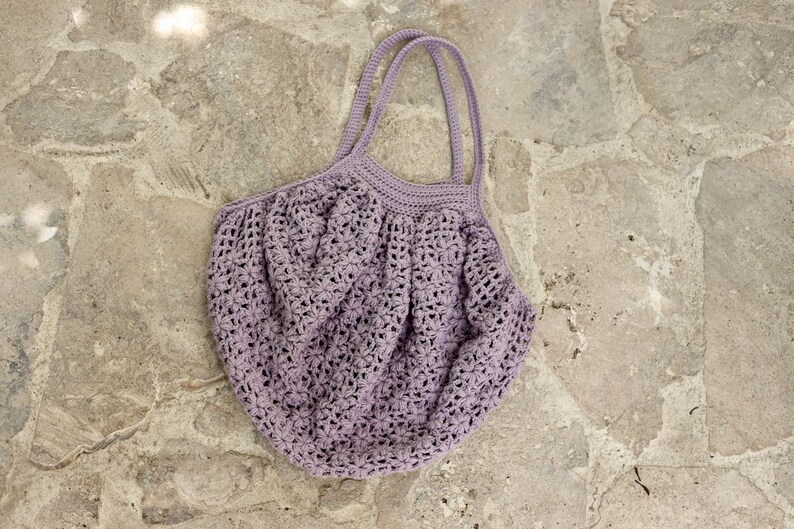 May include: A light purple crocheted tote bag with two handles. The bag is made of a delicate, open-weave pattern.