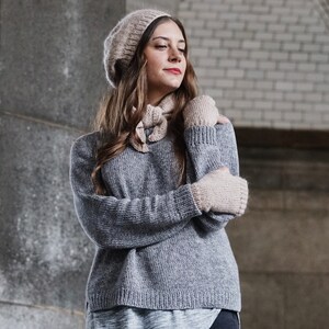 Puede incluir: Una mujer lleva un su&eacute;ter de punto gris, un gorro de punto beige y guantes sin dedos a juego. El su&eacute;ter tiene un corte holgado y una longitud ligeramente recortada. El gorro es de estilo beanie holgado. Los guantes son de un dise&ntilde;o sencillo con una textura acanalada.