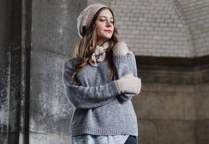 Puede incluir: Una mujer lleva un su&eacute;ter de punto gris, un gorro de punto beige y guantes sin dedos a juego. El su&eacute;ter tiene un corte holgado y una longitud ligeramente recortada. El gorro es de estilo beanie holgado. Los guantes son de un dise&ntilde;o sencillo con una textura acanalada.