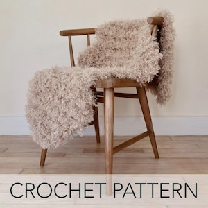 May include: A beige crochet throw blanket draped over a wooden chair. The blanket has a fluffy, shaggy texture.