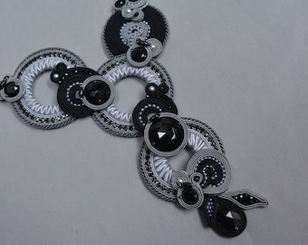 Puede incluir: Un collar negro y plateado con múltiples diseños circulares y acentos de piedras preciosas negras.