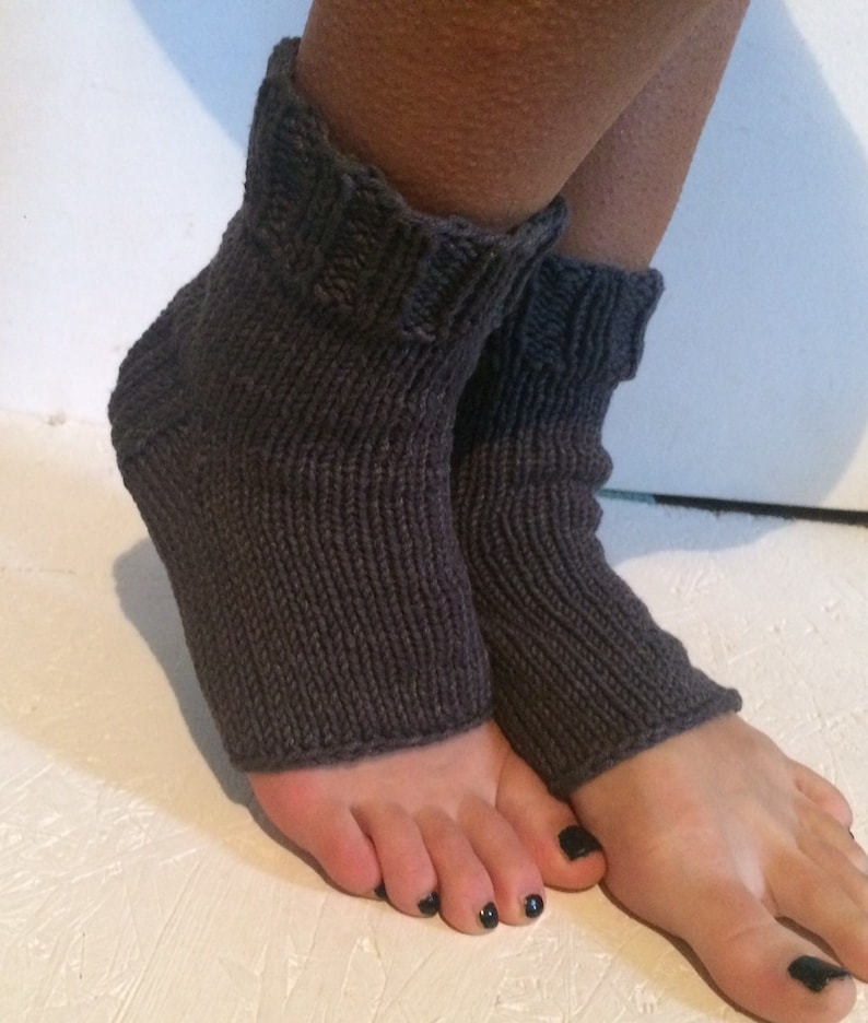 May include: Dark gray knitted foot warmers. These open-toe socks are made of a thick, textured yarn. The cuffs are folded over, and the socks cover the foot and ankle.