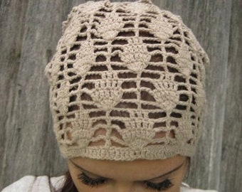 May include: A beige crochet hat with an openwork design. The hat features a repeating pattern of floral or leaf-like shapes, creating a delicate and airy texture. The hat is designed to be worn on the head.