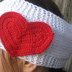 May include: A white crocheted headband with a large, red heart applique. The heart is also crocheted and is centered on the headband. The headband is a winter accessory, perfect for Valentine's Day or everyday wear.