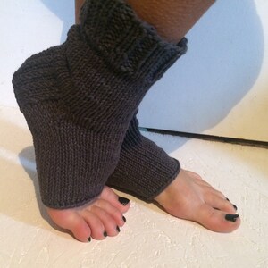 May include: Dark gray knitted leg warmers. The leg warmers are made of a thick, textured yarn and have a ribbed cuff at the top. The foot portion is open, and the leg warmers are designed to be worn over the foot and ankle.