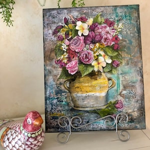 May include: A painting of a bouquet of pink, white, and purple flowers in a yellow ceramic vase. The vase is sitting on a textured, blue and green background. The painting is framed and ready to hang.