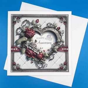 May include: A square anniversary card featuring a white quilted design and a heart-shaped frame decorated with roses, pearls, and clock motifs. The card displays the text "Happy Anniversary" and comes with a white envelope.