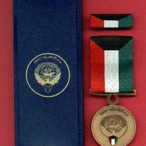 May include: A blue velvet box with a gold medal inside. The medal is round and features a green, white, and red flag with a gold eagle on top. The medal is surrounded by a gold rim and has the text "1991 - 2011" on the top.