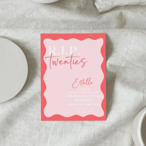 May include: A pink and coral invitation card with the text "R.I.P. Twenties" and event details. The card has a wavy coral border and is set on a neutral linen surface, with decorative bowls in the background.