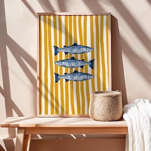 May include: A framed rectangular wall art print featuring three blue fish stacked vertically against a background of vertical mustard yellow and white stripes. The fish have a textured, mosaic-like appearance with dark outlines and varied blue tones.