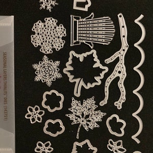 Pode incluir: Um conjunto de 15 formas de corte de metal para artesanato. As formas incluem flocos de neve, folhas, flores, um galho e uma borda ondulada. Os matrizes são prateadas e têm um acabamento brilhante.