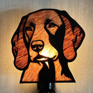 May include: A wall-mounted night light featuring a cutout silhouette of a dog head. The design is crafted from black material with a textured, warm-toned wood grain inlay that glows from within when illuminated, highlighting the canine facial features.