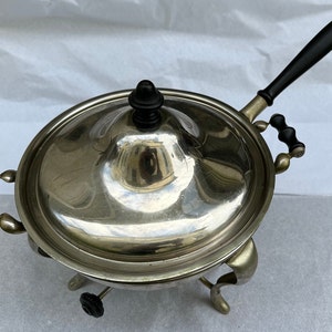 May include: Silver chafing dish with a black handle and black knob on the lid. The dish sits on three legs with black knobs.