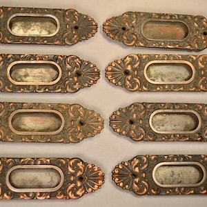 May include: Eight antique ornate brass door or drawer pulls with oval openings. The pulls have a decorative floral design and a copper patina.