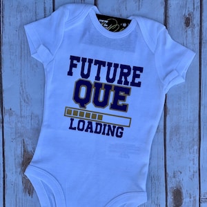 May include: White baby onesie with a blue and gold graphic that says "FUTURE QUE LOADING" with a progress bar.