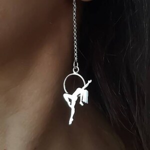 以下が含まれることがあります： 小さな円と輪っかからぶら下がっている人のシルエットが特徴のシルバー製のぶら下がりイヤリングです。