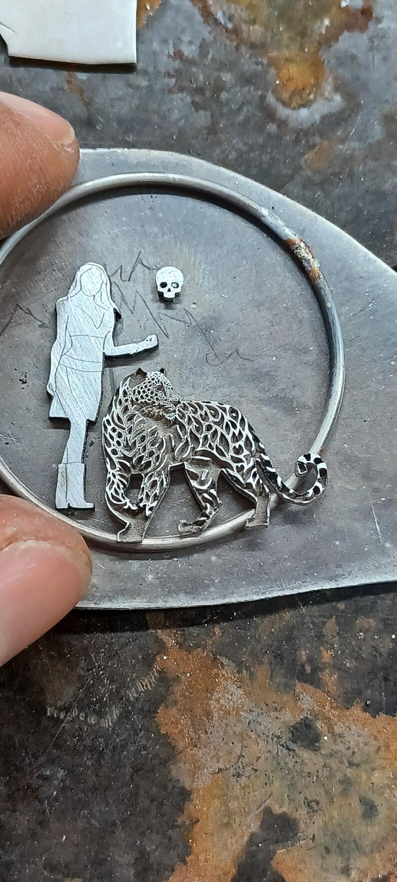 Puede incluir: Colgante de metal plateado con un dise&ntilde;o de mujer, leopardo y calavera. El leopardo est&aacute; intrincadamente detallado. El colgante est&aacute; sobre una superficie texturizada, con un marco circular.