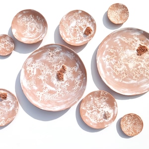 Puede incluir: Conjunto de ocho platos de cerámica de terracota con vetas blancas. Los platos son de varios tamaños y formas, algunos tienen un borde elevado.