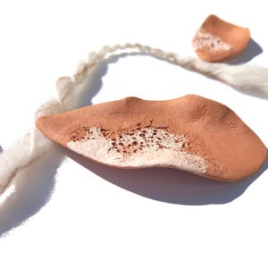 May include: A terracotta necklace with a white and brown speckled design. The necklace is made of clay and has a natural, organic look. The necklace is strung on a white cord.