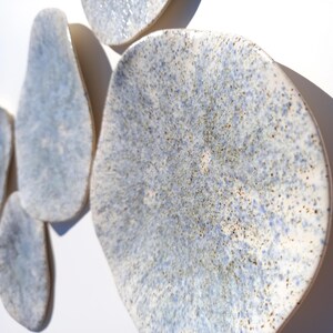 May include: A collection of irregularly shaped ceramic wall art pieces. The pieces have a speckled blue and white glaze with a textured surface. The shapes vary in size and are mounted on a white background.