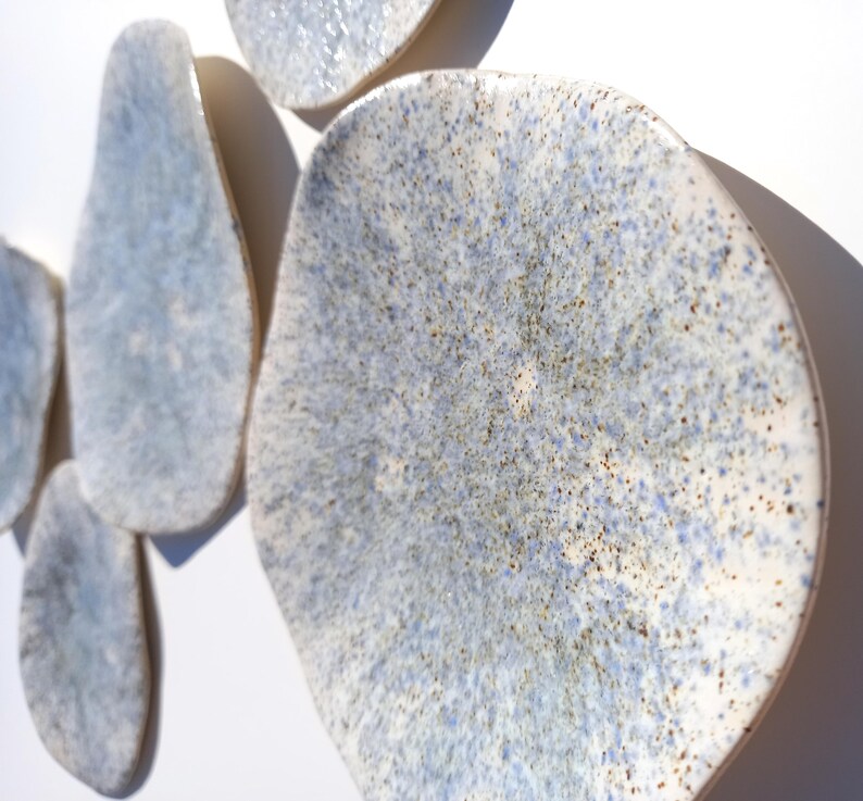 May include: A collection of irregularly shaped ceramic wall art pieces. The pieces have a speckled blue and white glaze with a textured surface. The shapes vary in size and are mounted on a white background.