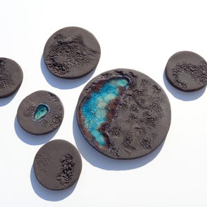 May include: A set of nine round ceramic wall decor pieces in shades of brown and blue. The pieces feature a textured surface and some have a blue glaze.