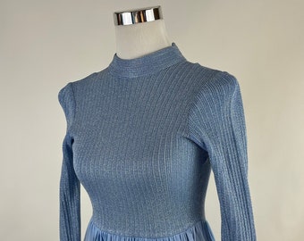Peut inclure: Une robe bleu clair à manches longues, col montant et jupe plissée. La robe est en tissu côtelé avec un léger effet brillant.