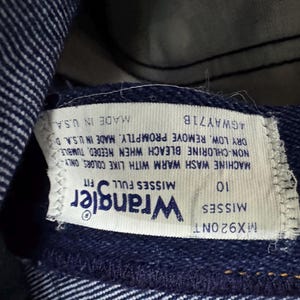 May include: Close-up of a blue denim Wrangler jeans label. The label reads "Wrangler" and "Misses Full Fit". The size is 10. The label also includes washing instructions and "Made in U.S.A."