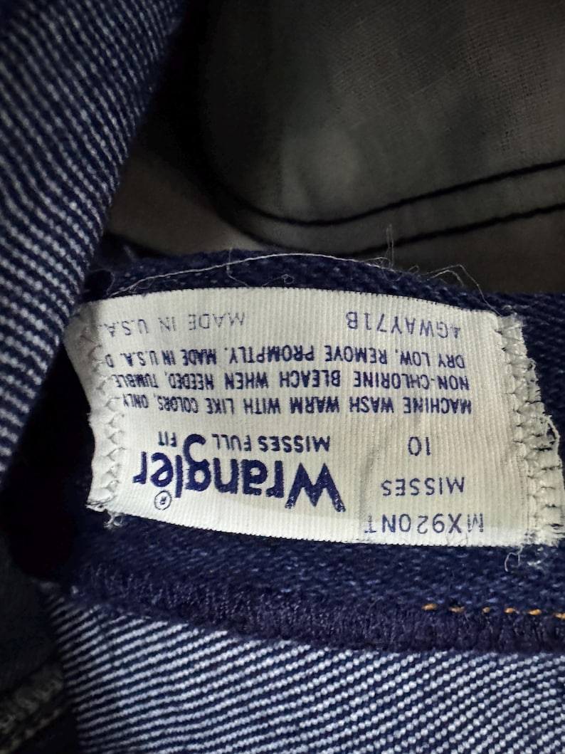 May include: Close-up of a blue denim Wrangler jeans label. The label reads "Wrangler" and "Misses Full Fit". The size is 10. The label also includes washing instructions and "Made in U.S.A."