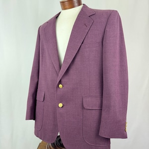 May include: A purple blazer with gold buttons, displayed on a mannequin. The blazer has two front pockets and a chest pocket. The fabric has a subtle texture. The blazer is a classic style.