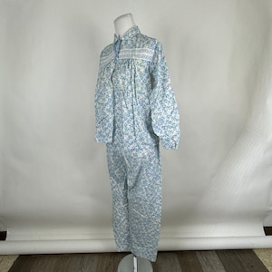 Peut inclure: Un ensemble de pyjama deux pièces sur un mannequin. L'ensemble présente un motif floral bleu clair sur fond blanc. Le haut a des manches longues et une fermeture boutonnée avec des détails brodés blancs. Le pantalon est droit.